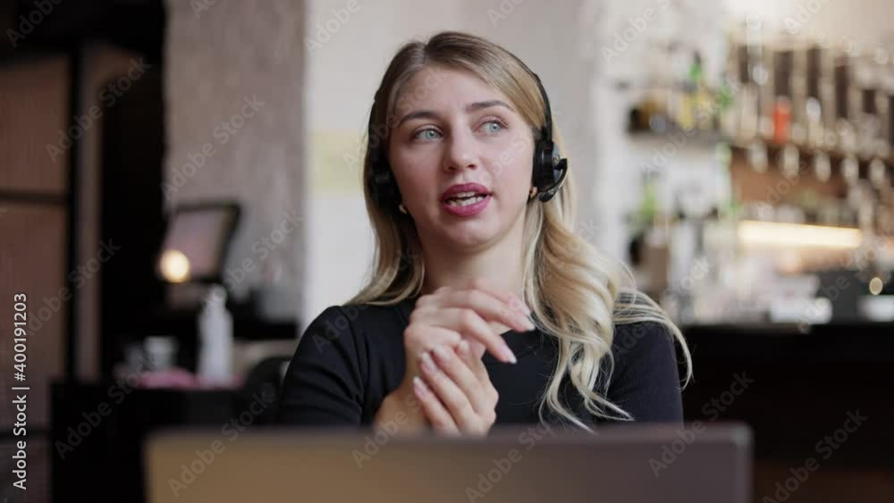Happy young business woman wears headset talks to web camera making distance online video conference call. Female internet teacher doing distant chat working from coffee house. job interview. Happy young business woman wears headset talks to web camera making distance online video conference call. Female internet teacher doing distant chat working from coffee house. job interview.
