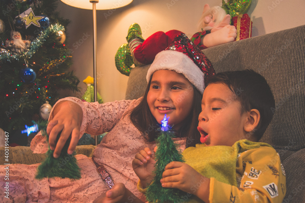 Escena infantil navideña. Niño y niña sentados en el sofá con el árbol ...