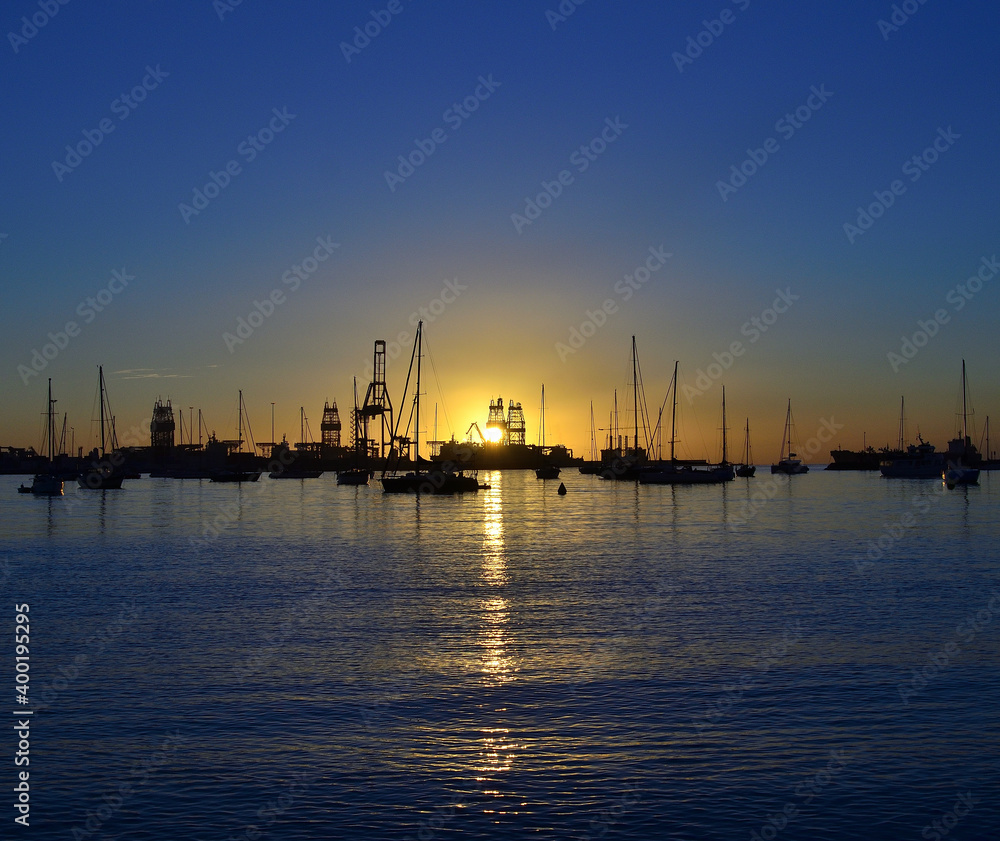 Sunrise in the bay with calm sea, intense blue sky and backlit port with many ships