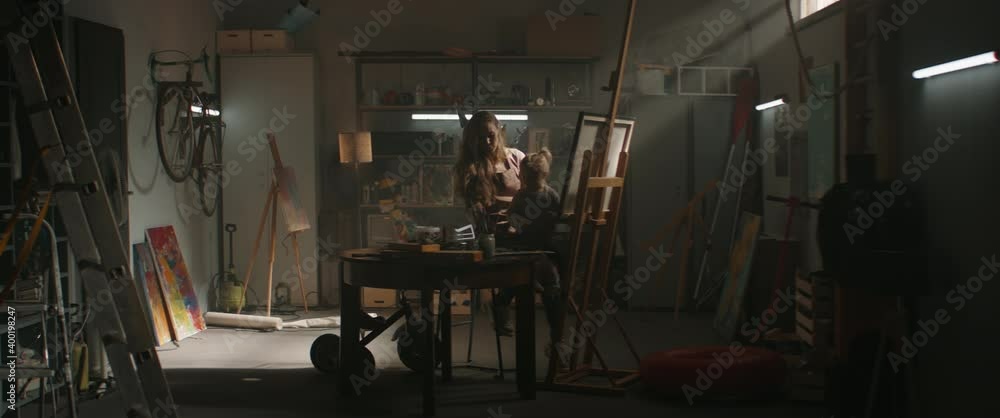WIDE Female painter artist working in studio inside her garage, little daughter helping with the picture. Shot with 2x anamorphic lens WIDE Female painter artist working in studio inside her garage, little daughter helping with the picture. Shot with 2x anamorphic lens