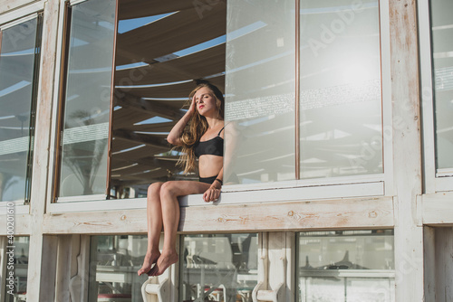 cute young teenage girl or woman posing and having fun on the beach cafe window under palm trees in summer swimsuit . Trendy girl posing. Funny and positive woman. © MartaKlos