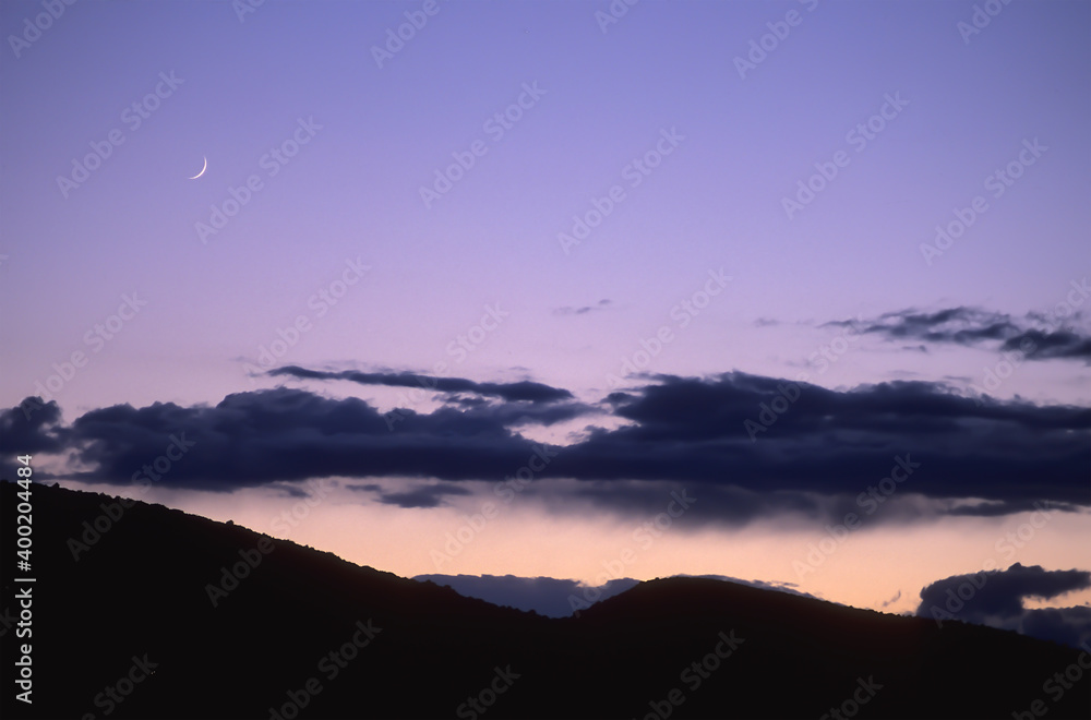 Clouds in the backlight of sunset over mountains with a waxing moon. Clouds in the backlight of sunset over mountains with a waxing moon.
