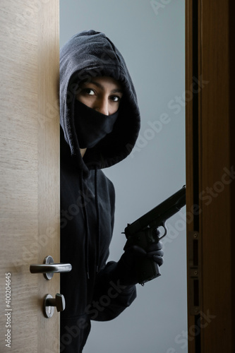 Thief broke into the apartment. House robbery by woman in a black jacket and black mask black gun and crowbar. Burglar in a mask. Thief in a mask trying to break into other people's house.