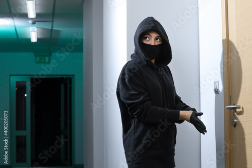 Thief broke into the apartment. House robbery by woman in a black jacket and black mask and crowbar. Burglar in a mask. Thief in a mask trying to break into other people's house