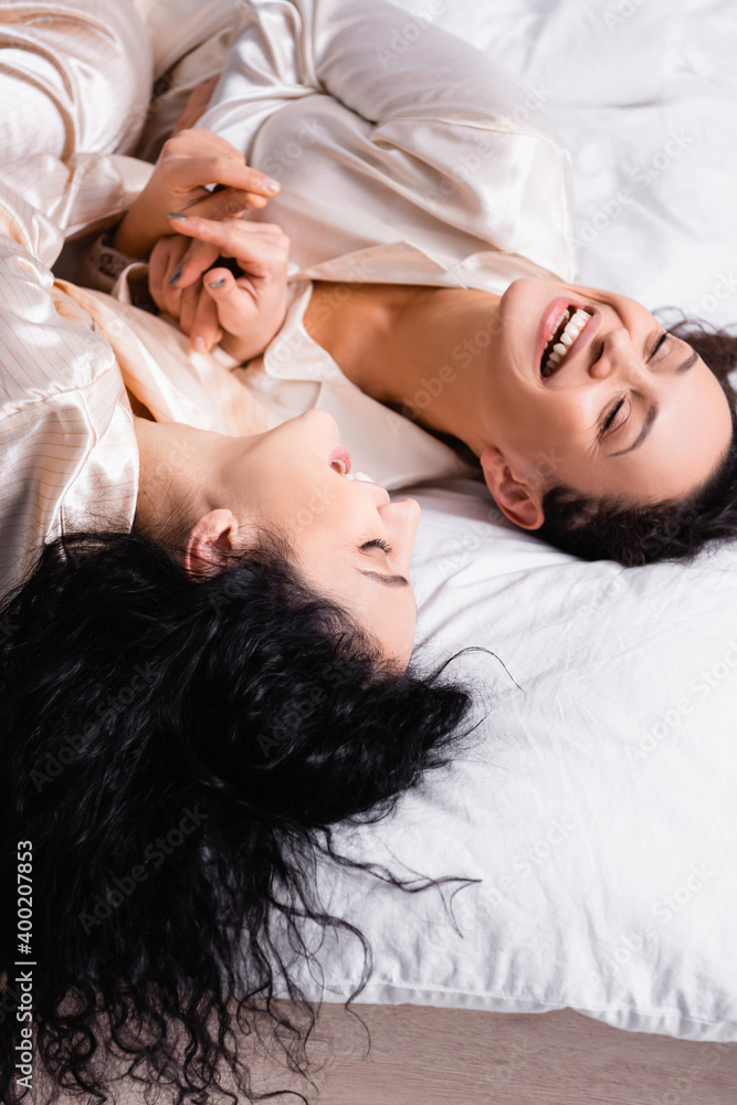 High angle view of cheerful Hispanic same sex couple laughing on bed at morning