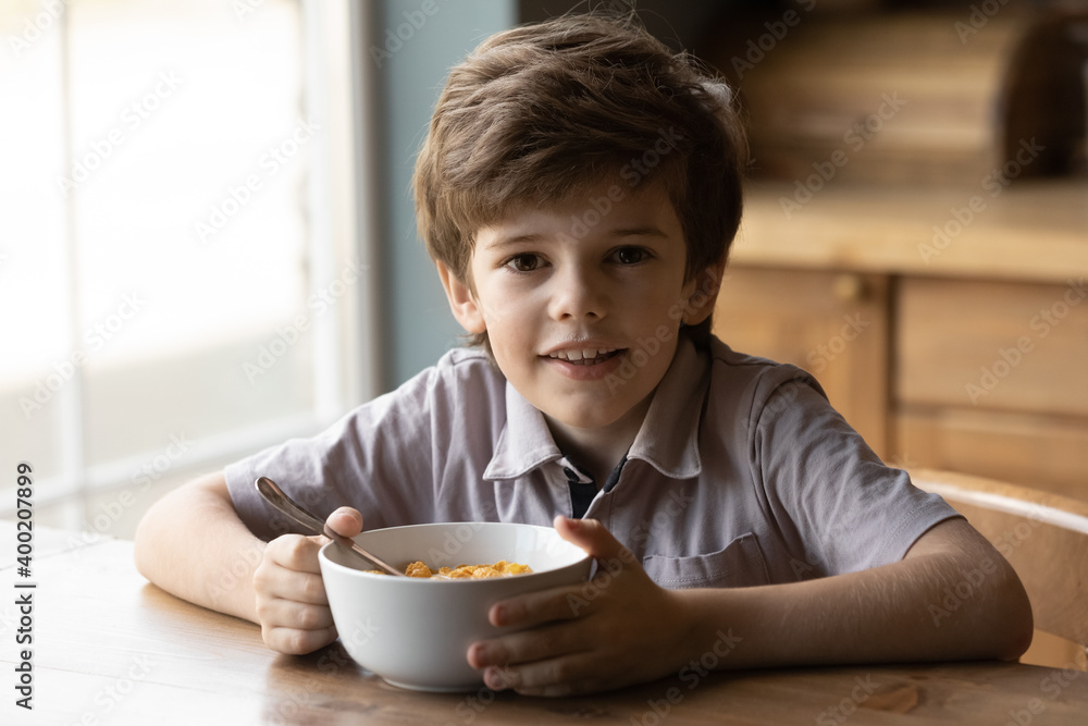Best breakfast ever. Portrait of adorable little boy looking at camera having healthy tasty snack. Small kid posing by kitchen table holding bowl of sugar coated cereal frosted corn flakes with milk Best breakfast ever. Portrait of adorable little boy looking at camera having healthy tasty snack. Small kid posing by kitchen table holding bowl of sugar coated cereal frosted corn flakes with milk