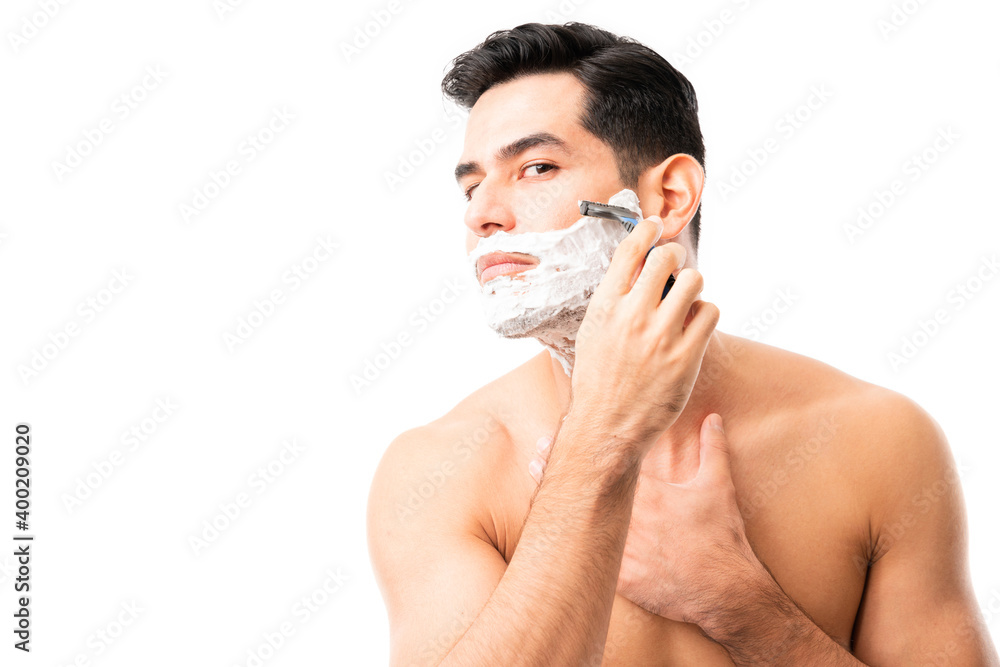 Hispanic male shaving is beard with razor