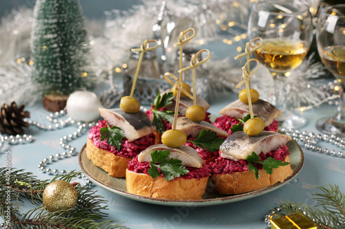 Canapes with salted herring, olives and beets on white bread croutons in a plate on a light blue background. Horizontal format. Closeup