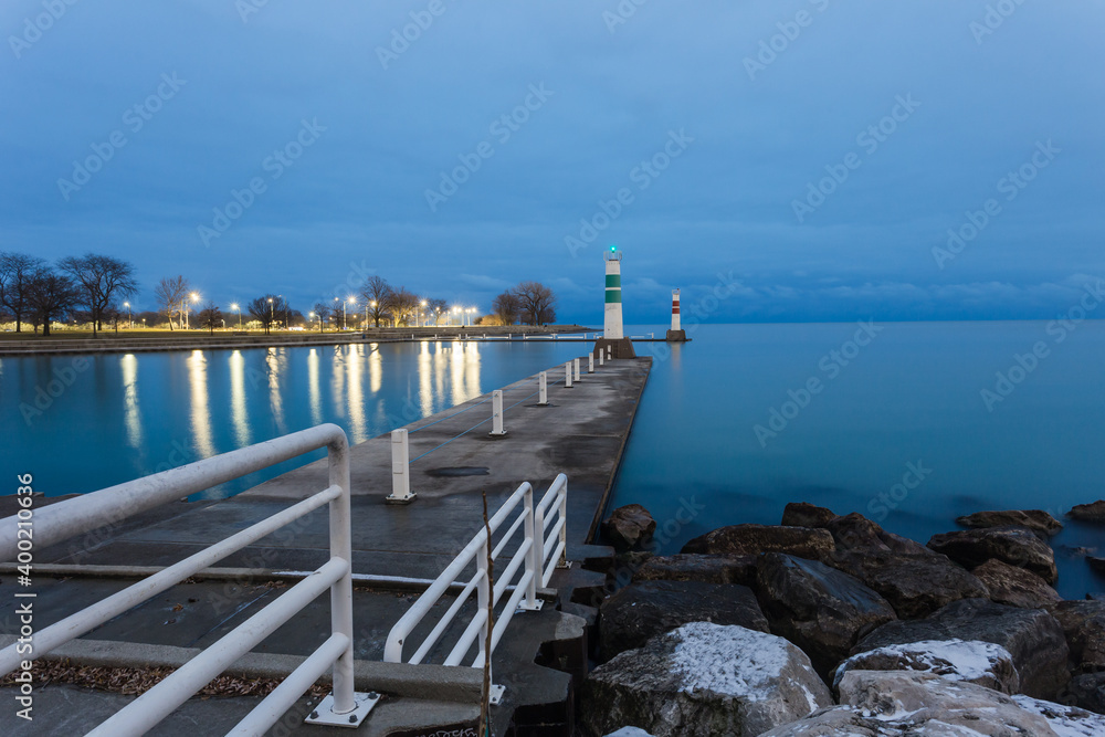 Concrete pier leading to boat entrance to lake Michigan with park in background with cloudy sky