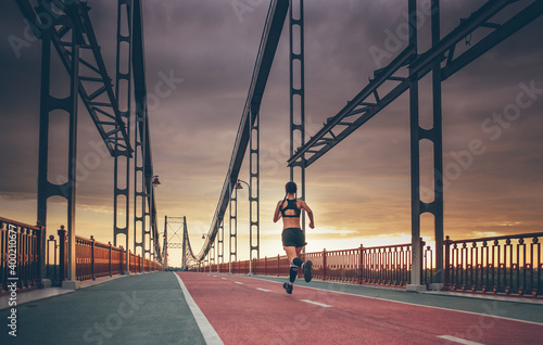 sporty female running outdoors on the bridge during sunrise