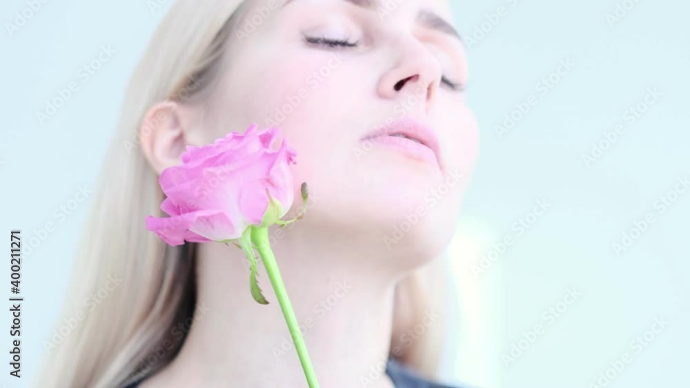 Beautiful young woman with delicate rose flower. Girl clean fresh skin touching her face in flowers. Slow motion video. stock footage Beautiful young woman with delicate rose flower. Girl clean fresh skin touching her face in flowers. Slow motion video. stock footage