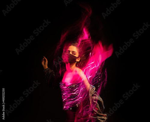 Face mask party mood. Beautiful young woman in fancy shiny festive outfit black background. Long exposure artistic creative dynamic motion effect. quarantine restrictions covid time party running away