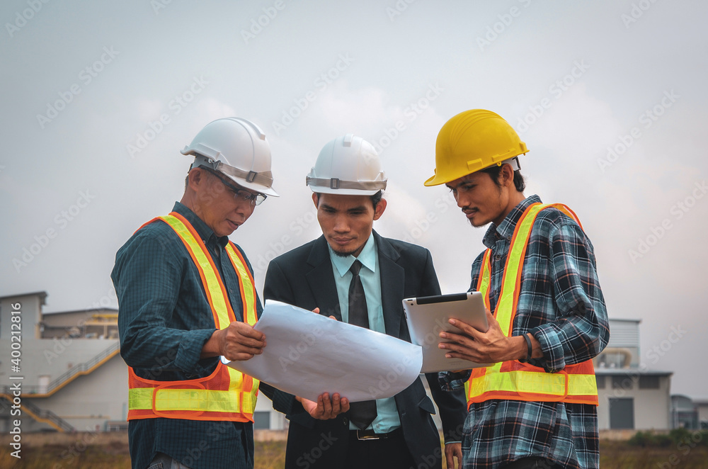 Construction engineers speak at the construction site, with a tablet and blueprint in the hand.