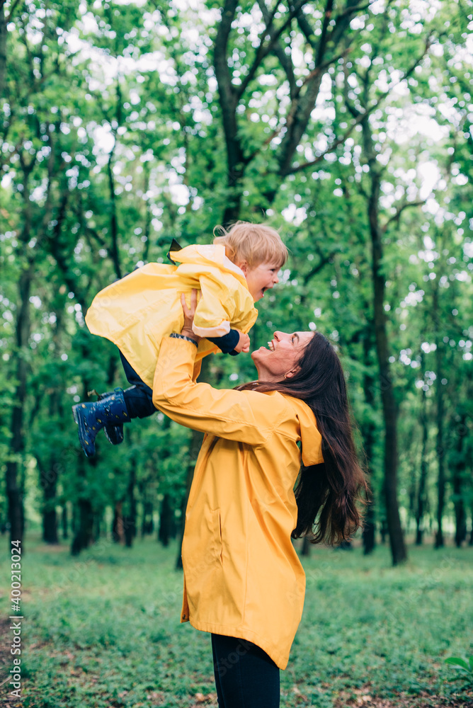 young mother with her son in yellow rain jackets playing outdoors in park after the rain. Family in park playing together and having fun. young mother with her son in yellow rain jackets playing outdoors in park after the rain. Family in park playing together and having fun.