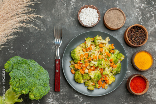 Top view of set of different spices in brown bowls and vegetable salad with fresh broccoli