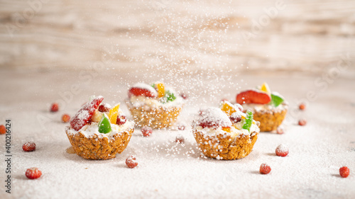 Sprinkling icing sugar over healthy cupcakes with cottage cheese, strawberries, banana, dried fruits. Winter background