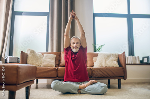 Grey-haired man sitting on the floor and doing yoga photo
