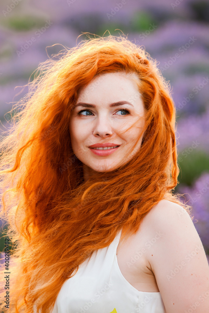 Summer portrait of a beautiful girl with long curly red hair. European girl in lavender field. Wavy Red Hair Summer portrait of a beautiful girl with long curly red hair. European girl in lavender field. Wavy Red Hair
