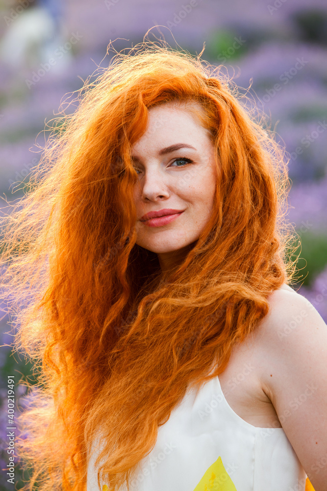 Summer portrait of a beautiful girl with long curly red hair. European girl in lavender field. Wavy Red Hair Summer portrait of a beautiful girl with long curly red hair. European girl in lavender field. Wavy Red Hair