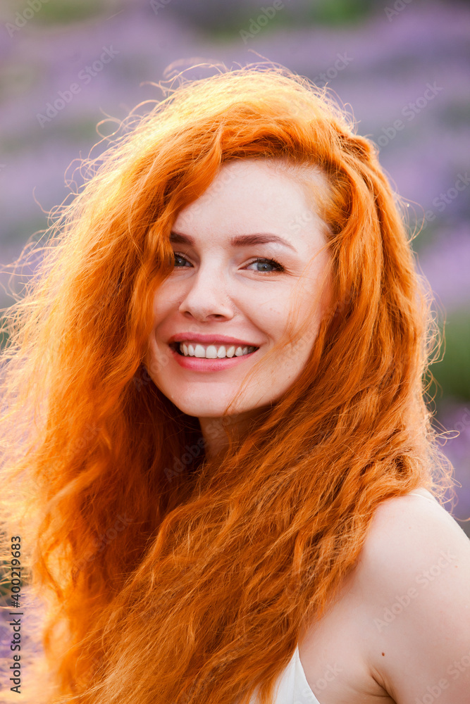 Summer portrait of a beautiful girl with long curly red hair. European girl in lavender field. Wavy Red Hair Summer portrait of a beautiful girl with long curly red hair. European girl in lavender field. Wavy Red Hair