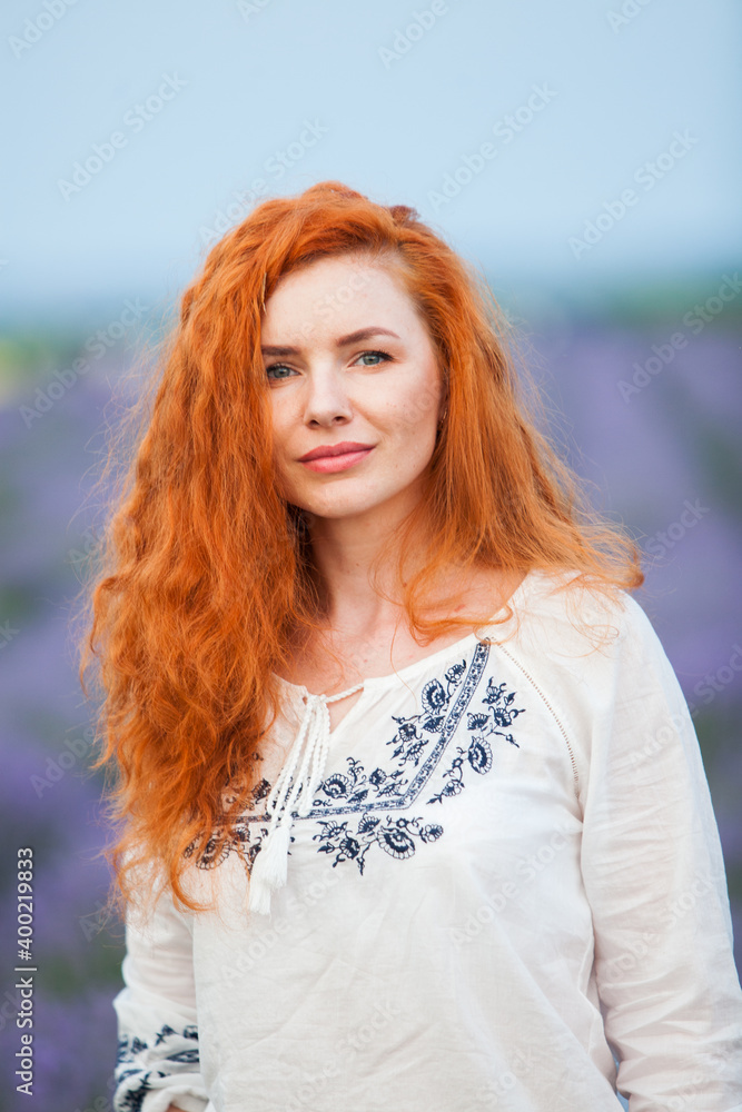 Summer portrait of a beautiful girl with long curly red hair. European girl in lavender field. Wavy Red Hair