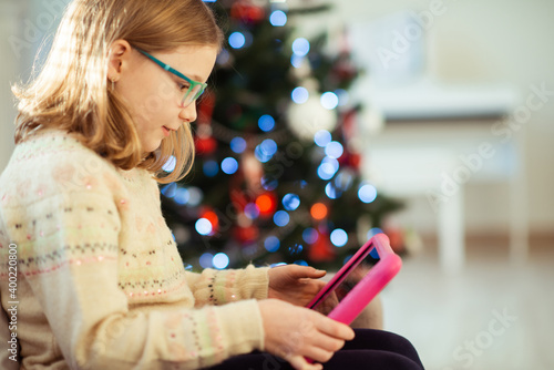 Cute little child girl playing with tablet near christmas tree