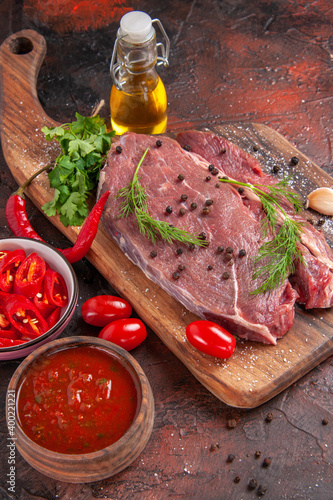 Above view of red meat on wooden cutting board and garlic green chopped pepper fallen oil bottle on dark background