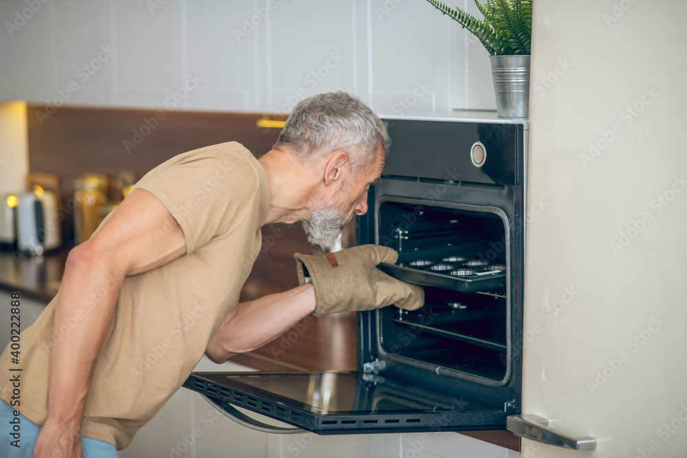 Mature man in beige tshirt taking something out the oven