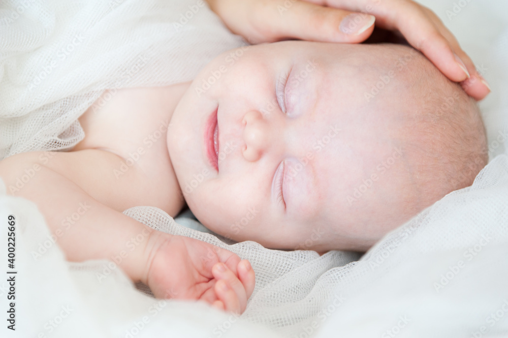 A smiling baby newborn boy with blue eyes smiles and crawls on a white sheet. A smiling baby newborn boy with blue eyes smiles and crawls on a white sheet.