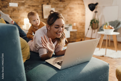Happy single mother waving during video call over laptop at home. © Drazen