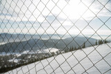 Ski resort closure concept, mountains behind bars, mesh netting, snowy peaks sunny day