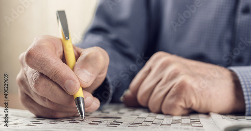 Aduld man with wrinkled skin writing letters with right hand in crossword in newspaper photo