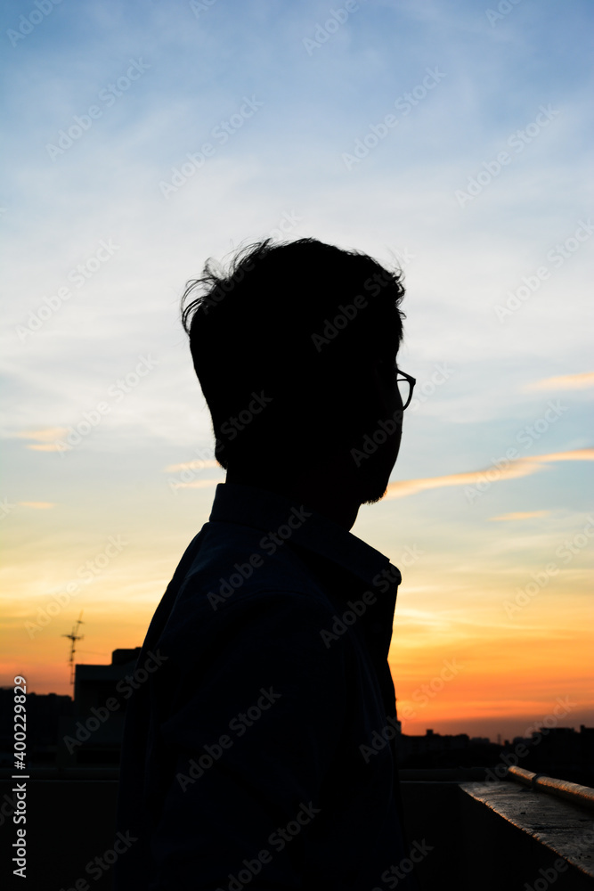 Silhouette of a lonely man standing on the roof top of the building in sunset background.