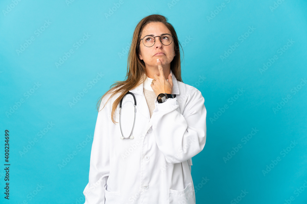 Middle age Brazilian doctor woman isolated on blue background having doubts while looking up Middle age Brazilian doctor woman isolated on blue background having doubts while looking up