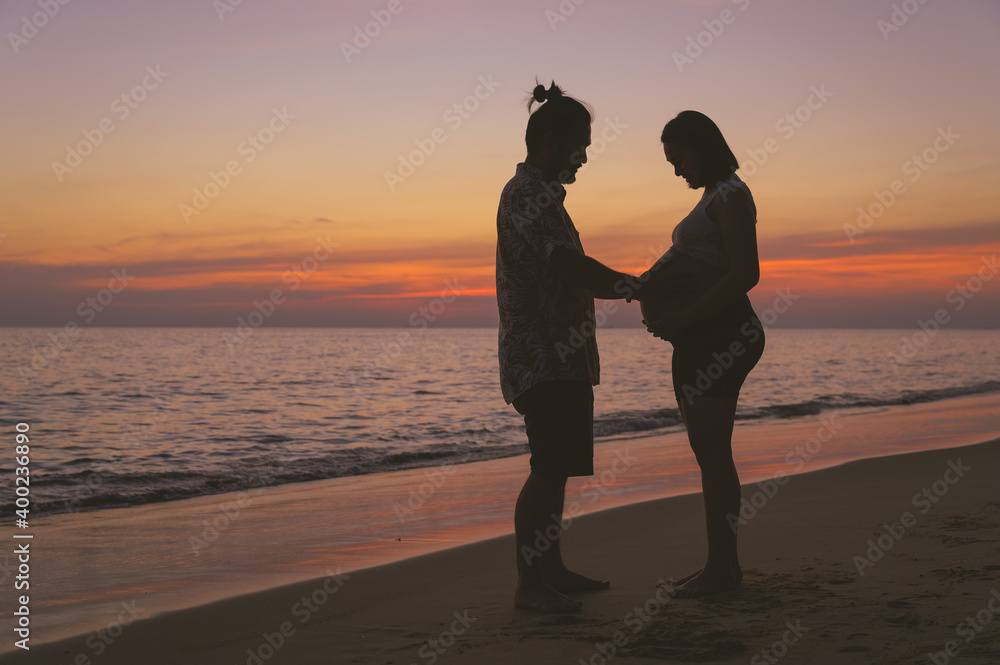 Young family and pregnant wife spend holiday on the beach at sunset.
