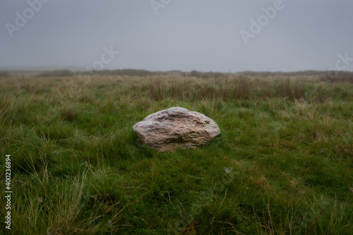 Single big granite stone in the field on rainy, misty and foggy day.