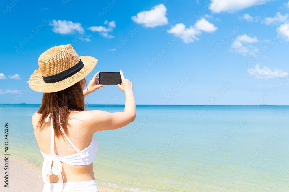 Asian woman in bikini enjoys summer vacation photographing beautiful sea in Thailand