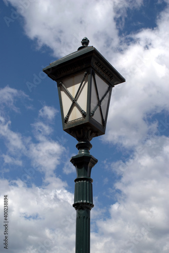 Black and white lamp post with street lantern in retro style in front blue sky with white clouds on bright sunny day vertical view closeup