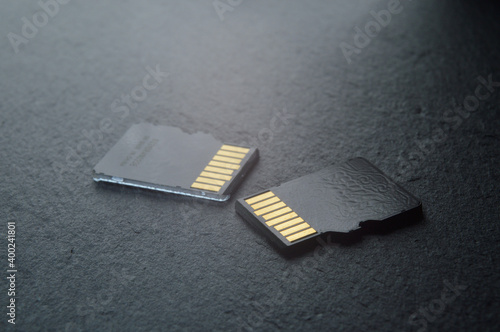 two micro sd cards lie on a dark textured background, with golden contacts at the top. close-up.