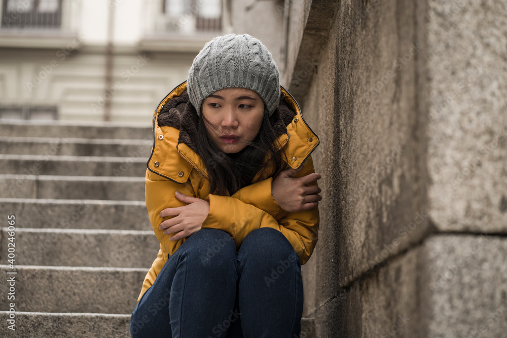 dramatic lifestyle portrait of young attractive sad and depressed Chinese woman in winter hat sitting outdoors on street corner staircase suffering depression problem crying dramatic lifestyle portrait of young attractive sad and depressed Chinese woman in winter hat sitting outdoors on street corner staircase suffering depression problem crying