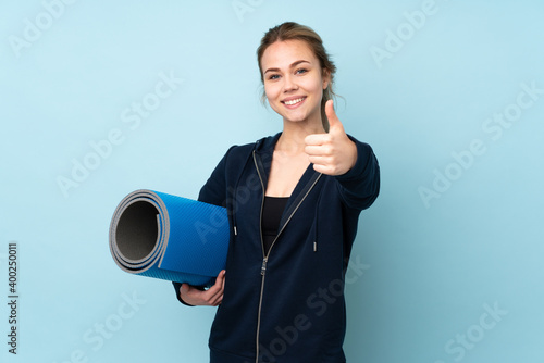 Teenager Russian girl holding mat isolated on blue background with thumbs up because something good has happened