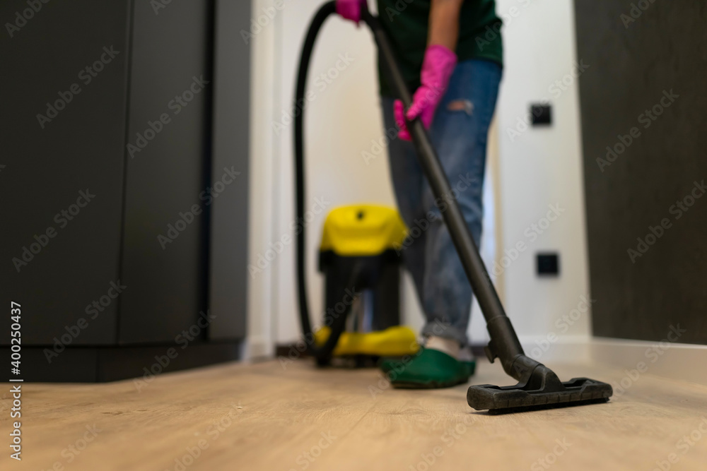 Fototapeta premium Woman vacuuming the parquet floor in the room with professional vacuum cleaner. Cleaning company employee cleans the house