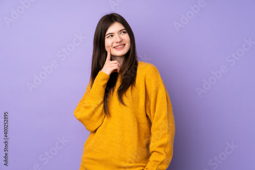 Young Ukrainian teenager girl over isolated purple background thinking an idea while looking up