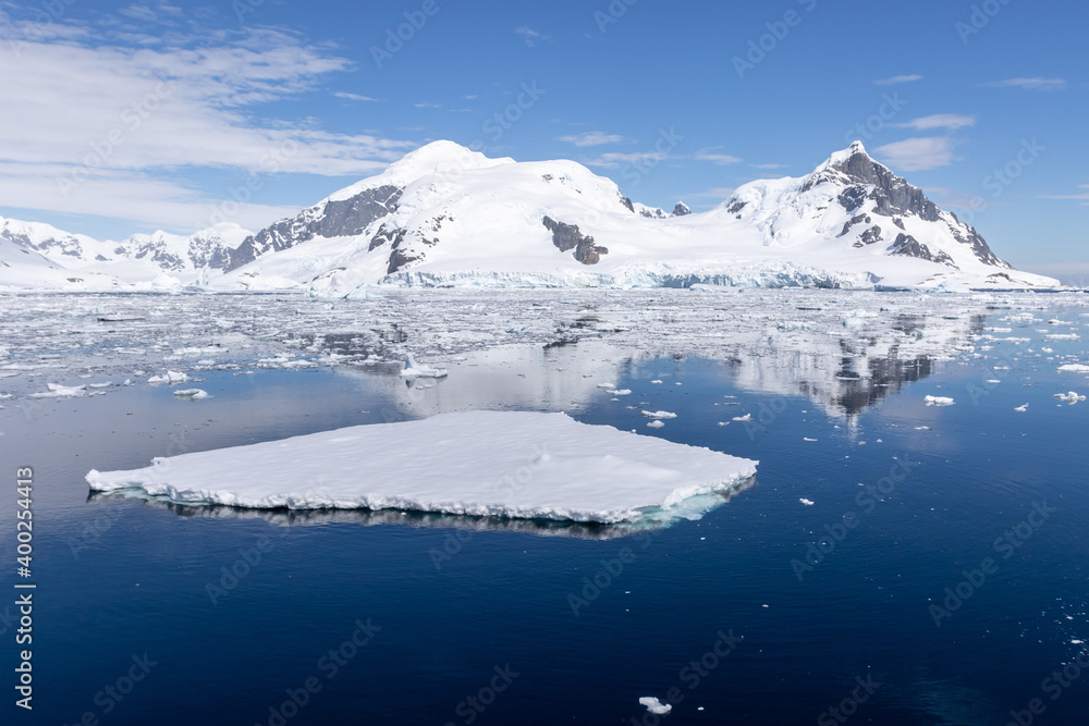 Flat small iceberg in calm water with mountains in the background in Antarctica.