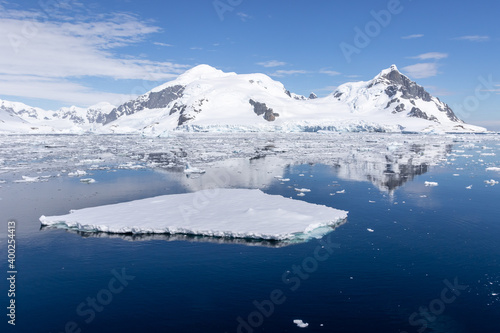 Flat small iceberg in calm water with mountains in the background in Antarctica.
