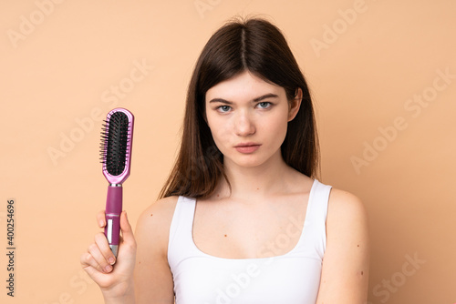 Young Ukrainian teenager girl over isolated background with hair comb