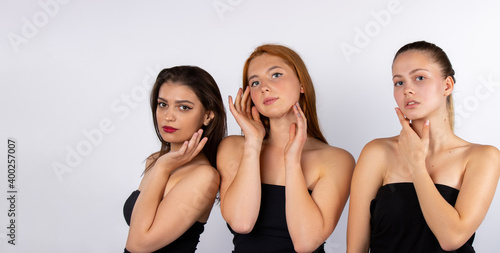 Three beautiful girls in black bodysuits posing on a white background in the studio. Spa and beauty concept