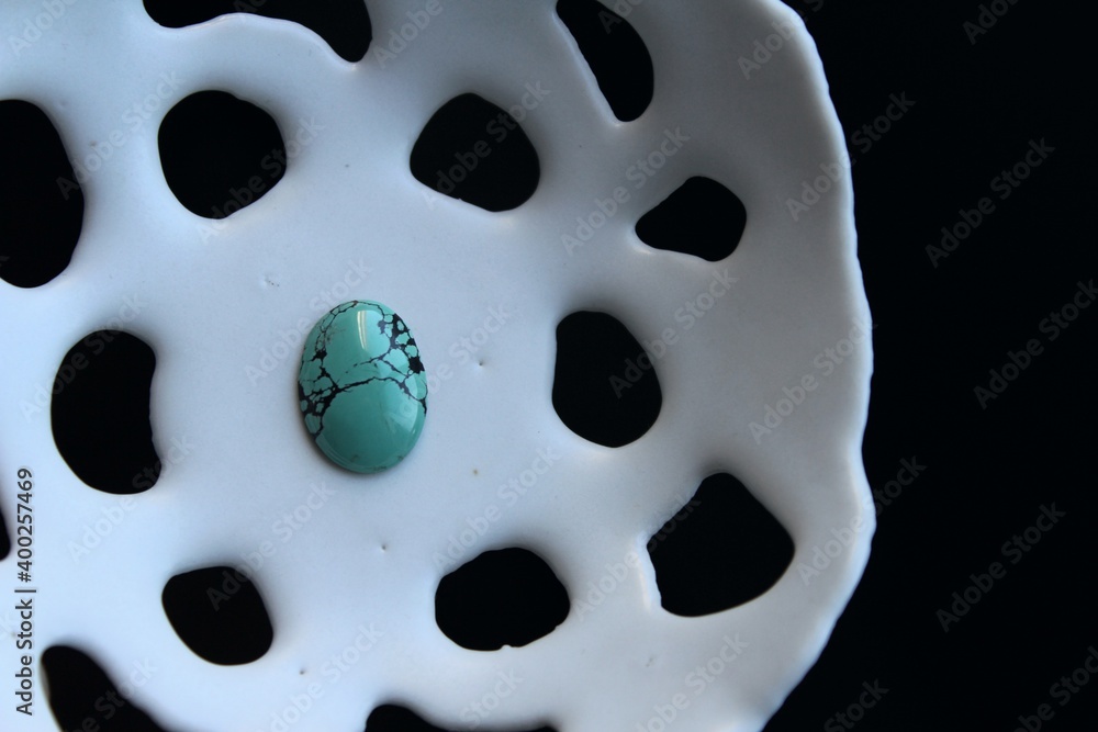 Natural stone for jewelry design, beautiful blue and green polished turquoise cabochon ready to be set into a silver jewellery piece, exposed on white porcelain plate. Natural stone for jewelry design, beautiful blue and green polished turquoise cabochon ready to be set into a silver jewellery piece, exposed on white porcelain plate.