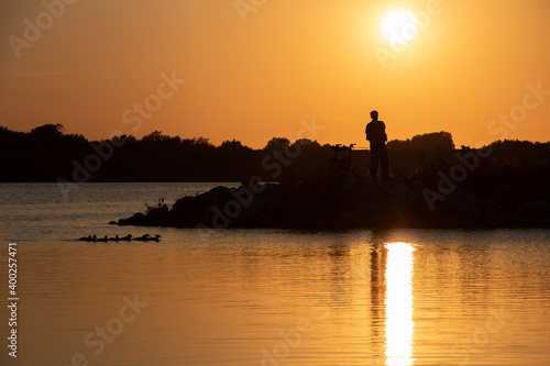 Man fishing during sunset with some ducks swimming