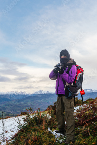 vertical photograph of a hiker and a photographer with a lot of warm clothes and a covered head to fight the cold.